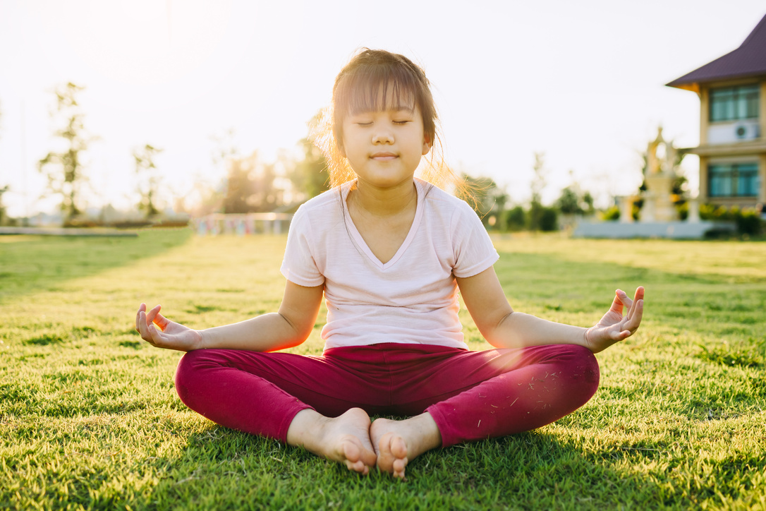 Children meditation with yoga pose on green grass field.